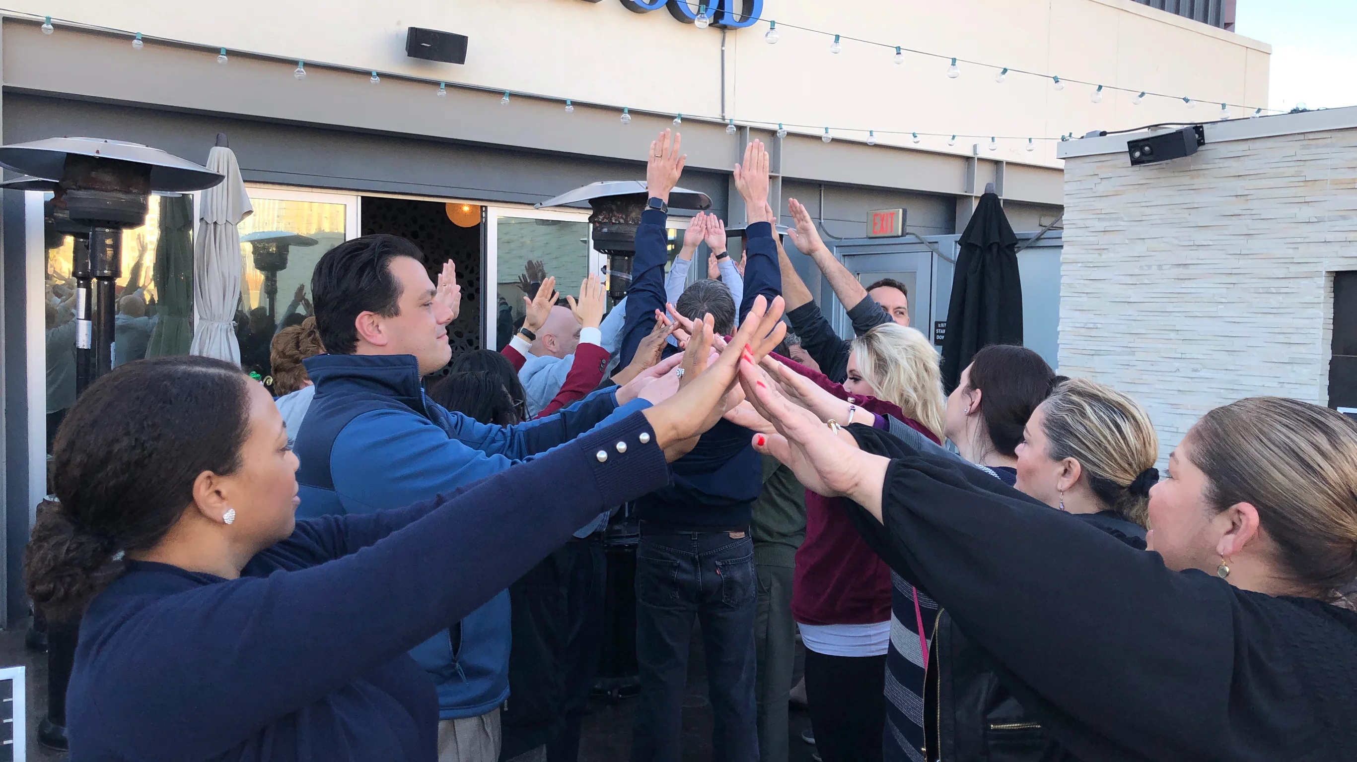 A group of professionals reaching hands together in a unified huddle during an applied improv workshop