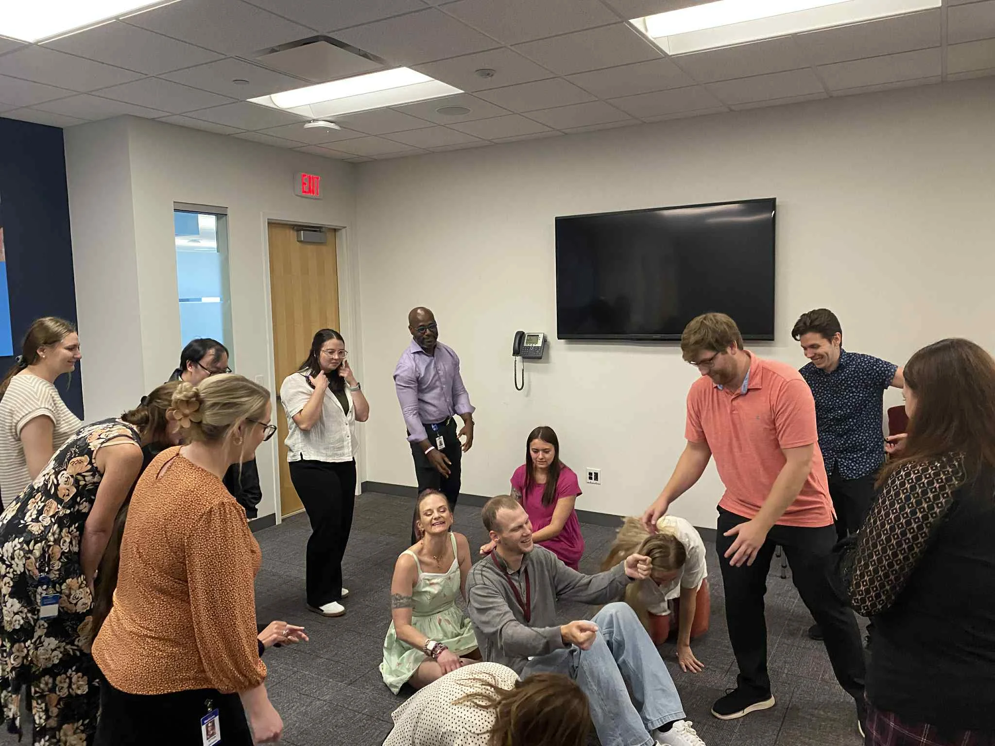 A diverse group of professionals laughing and engaging in an applied improv workshop exercise in a modern office